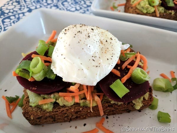 Beet and avocadoes on a toasted bread with a poached egg and pepper on top.