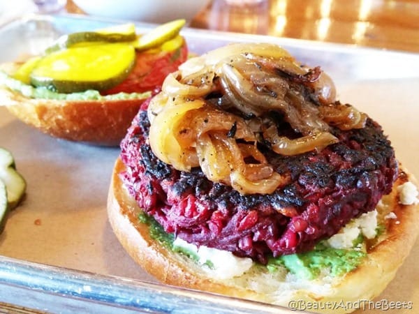 a red beet burger patty on a bun with sauteed onions and bread and butter pickles