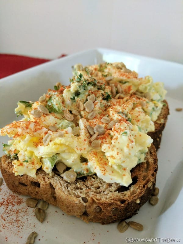large picture of creamy egg salad with sunflower seeds on a white plate red placemat
