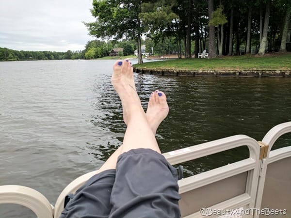 feet with pruple polish hab=nging over the side of a boat on a lake with lots of trees in the background