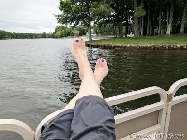 feet with pruple polish hab=nging over the side of a boat on a lake with lots of trees in the background