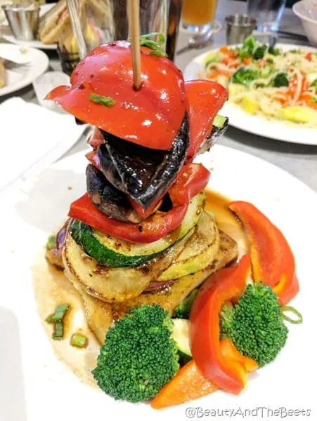 a stack of colorful vegetables inv=cluding squash zucchini red peppers and mushrooms on a white plate