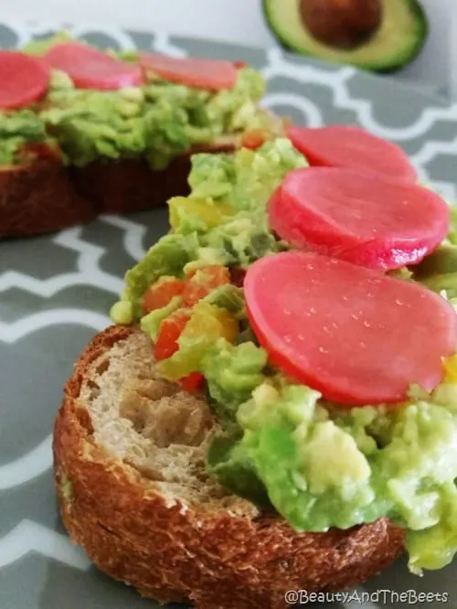 Toast topped with mashed avocado and bright pink pickled beets on a gray plate