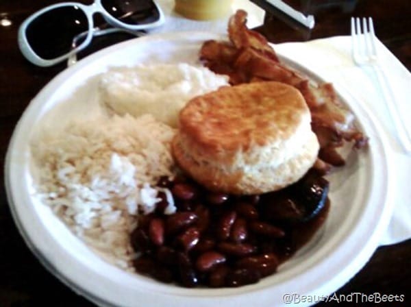 white plate with white rice, red beans, a biscuit and bacon on a table with a pair of white rimmed sunglasses next to the plate