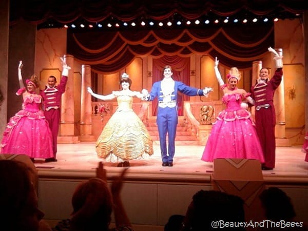 Belle in a gold ball gown, pink ball gowns, the Prince in a blue suit on stage