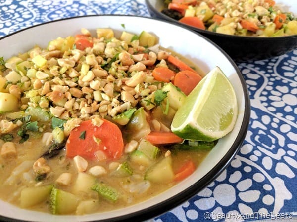 a bowl of broth with carrots, zucchini, peanuts and a lime wedge in a white and black striped bowl on a blue and white placemat