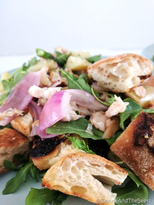 purple onions over bright greens and asparagus with large pieces of garlic bread croutons on a blue plate