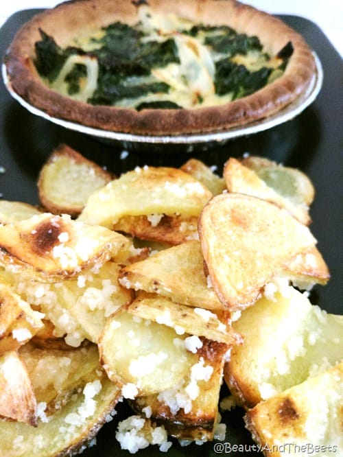 a pile of potatoes and garlic chips with an egg and kale pie tart in the bakcground on a black plate