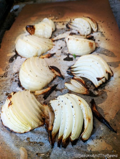 a baking sheet with roasted onion wedges on parchment paper