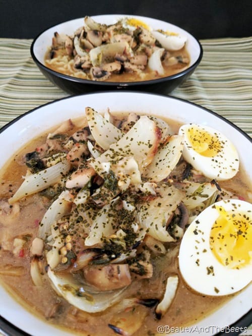 a bowl of noodle soup with onions and soft boiled eggs in a white bowl on a green striped placemat