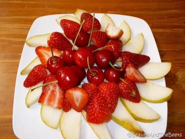 a square white plate with a pile of pear slices, cherries and sliced strawberries on a wooden table