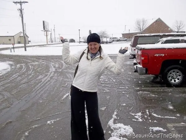 the author posing in a snowy parking lot wearing black pants, white jacket and black knit cap