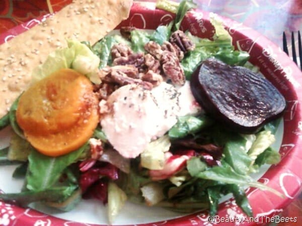 a red plate with gold and red beet slices, goat cheese and lettuce with a sesame cracker