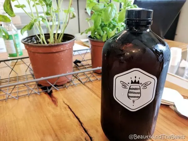 a single growler with bee logo in front of a pair of small potted plants