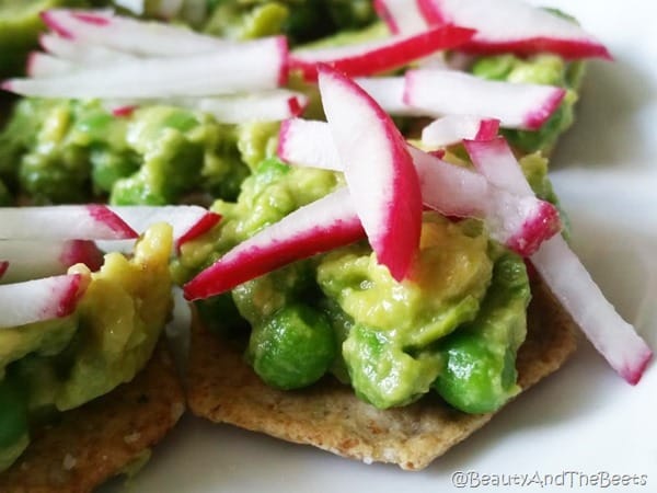 a cracker topped with peas and avocado and topped with shredded radishes