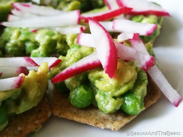 a plate of crackers with peas and avocado spread topped with shredded radish