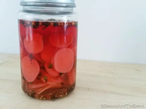 a jar of pickled bright pink radish on a wooden table with a white background