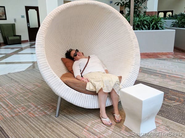 picture of the author wearing a yellow skirt and a white sweater in a white wicker pod chair