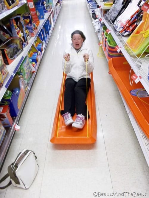 the author sledding in the middle of an aisle in a store on an orange sled screamming