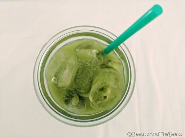 an overhead view of a glass of green matcha lemonade over ice with a long green straw on a white background