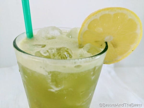 a glass of green matcha lemonade over ice with a green straw and a lemon slice on a white background