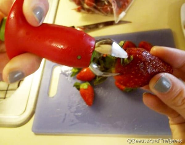 action shot of the huller being pushed into the top of a strawberry