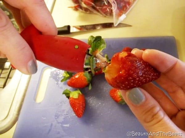 the huller pulling out the stem of the strawberry against a kitchen counter