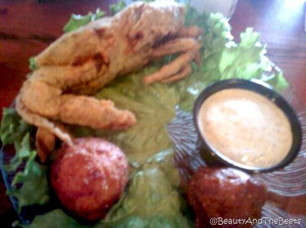 a soft shell crab on a bed of lettuce with red potatoes and a cup of cajun aoli