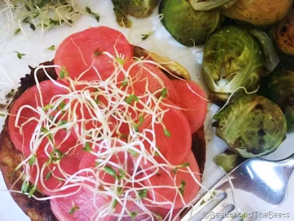 a veggie burger topped with bright pink pickled radish and a side of brussels sprouts on a white plate