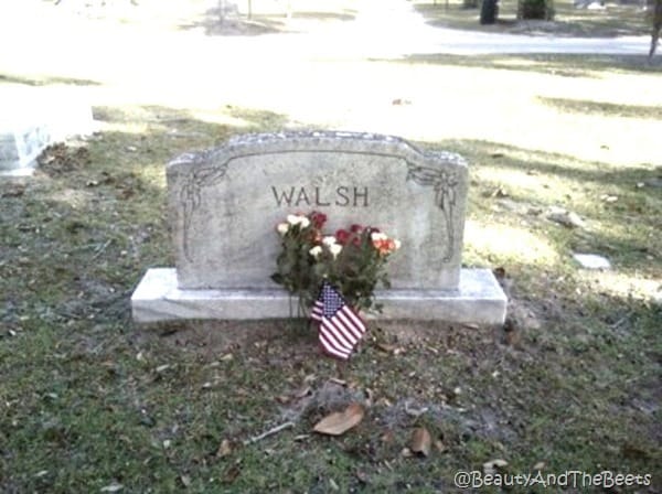 a granite headstone with the Walsh name with an AMerican flag and a bouquet of flowers in front of it