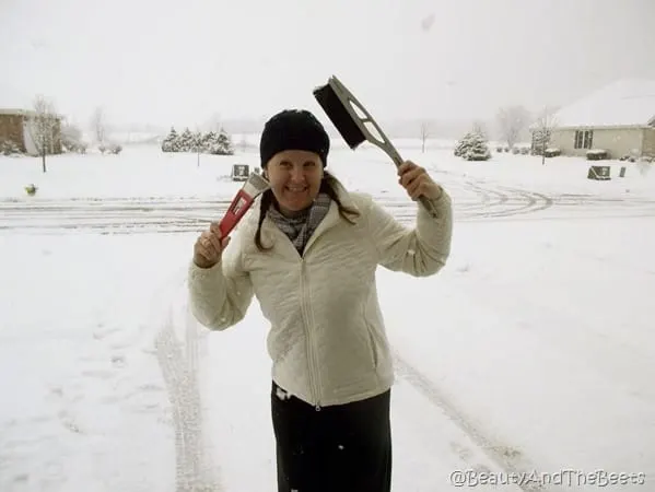 the author wearing a white jacket and black cap playing with a snow scraper and snow brush with a snowy background