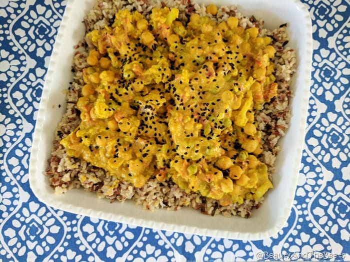 an overhead picture of vegetable curry and rice in a white square dish on a blue and white patterned placemat