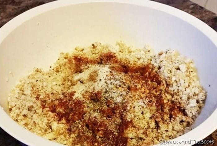 a white bowl filled with cauliflower and walnuts crumbles topped with brown and red spices