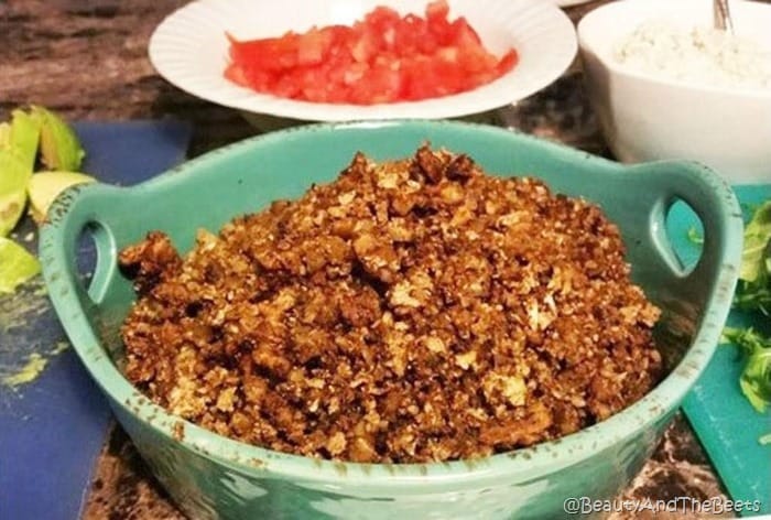a turquoise bowl filled with cauliflower walnut crumbles with a white bowl of chopped tomatoes in the background