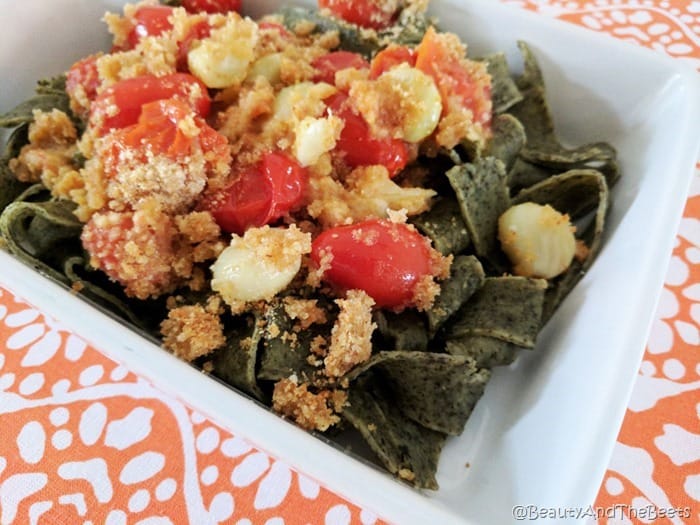 Green spinach pasta topped with roasted and blsitered tomatoes and garlic with breadcrumbs on a white plate on an orange placemat