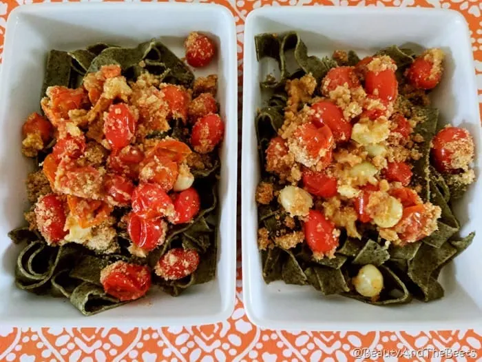 2 rectangular white dishes filled with spinach pasta, roasted tomatoes, garlic and breadcrumbs on an orange placemat