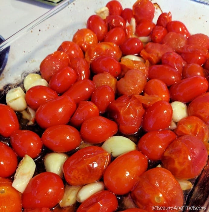 a glass casserole dish filled with blistered tomatoes and garlic
