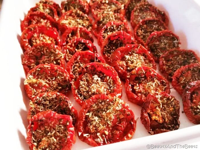 4 rows of sliced slow roasted wrinkled tomatoes filled with herbs and seasonings in a white casserole dish