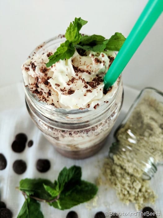 a mason jar filled with a midnight mint mocha frappuccino, whipped cream and a mint leaf with a green straw on a white tablecloth
