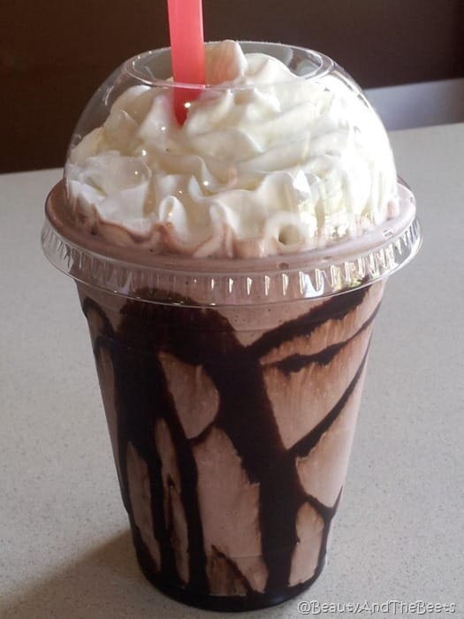 a plastic dome cup with a frozen chocolate beverage with chocolate syrup and whipped cream with a red straw