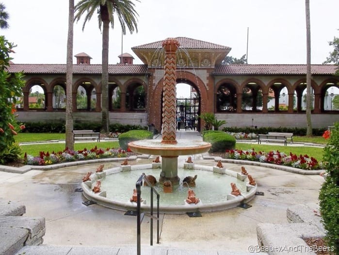 a two tier fountain in a courtyard with spanish tile and a gate with arches