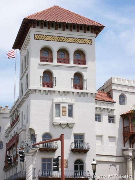 a stark white building with a tower and a spanish tile roof with a balcony and an American flag flying in the background against a blue sky