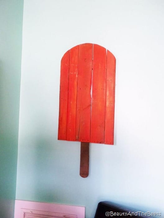 an artpiece made with wood of a red popsicle against a white wall