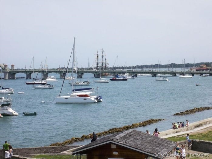 a scattering of boats on the sea with a long bridge in the background