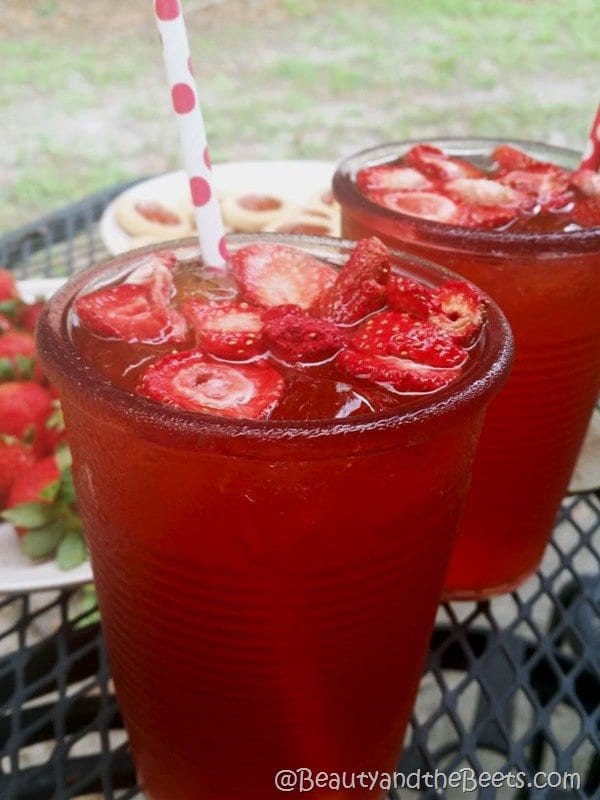 A red iced drink with strawberries and a red and white polka dotted straw on an outdoor table