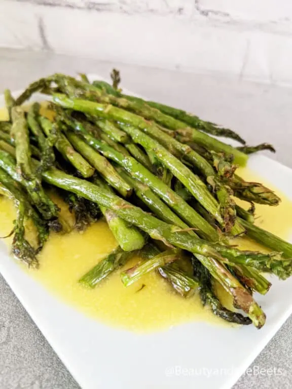 a pile of air fryer asparagus spears on a white plate with hollandaise sauce