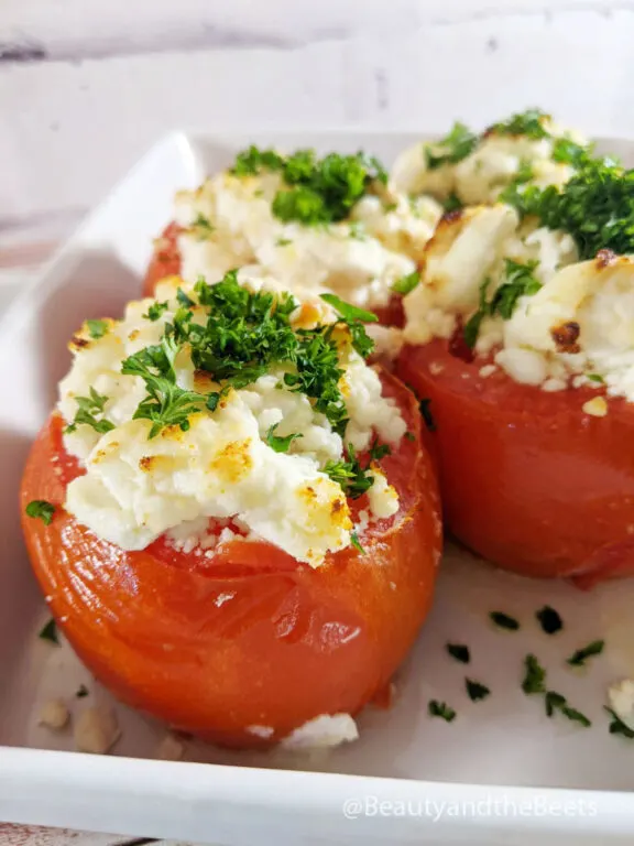 A white plate with four baked tomatoes with goat cheese topped with bright green parsley