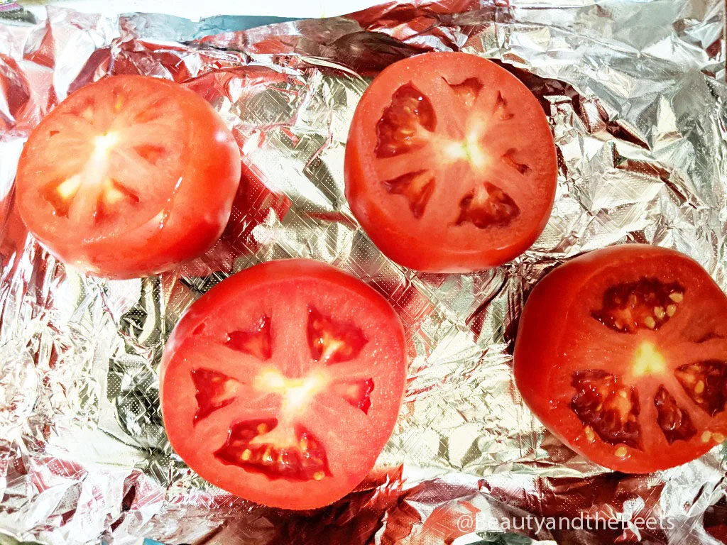 an overhead shot of four tomato halves on aluminum foil
