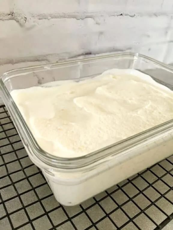 a rectangular glass dish of white orange ice cream recipe on a black grid rack on a gray stone tablestop